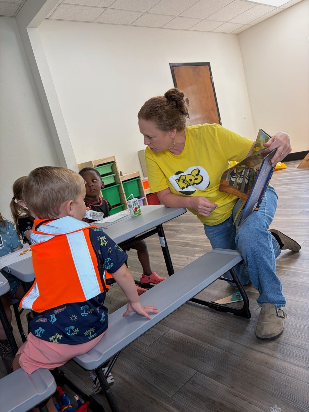 A kids volunteer reading a Bible story to toddlers