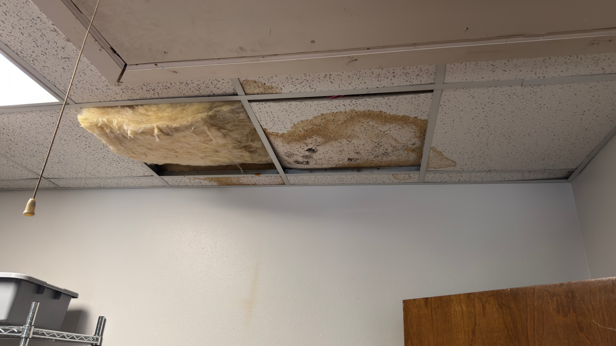 Water-damaged ceiling tiles and fallen insulation from a roof leak